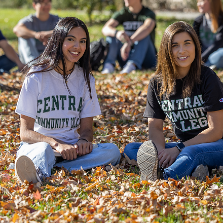 Two female students sitting on grass in the fall.