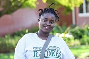 Female student on campus wearing a Central Community College Raiders t-shirt and smiling at the camera