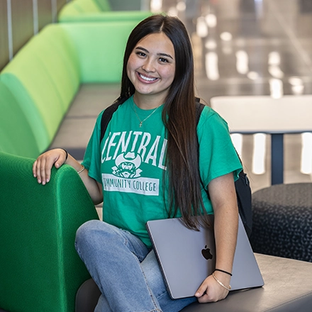 Female student in green tee shirt holding closed laptop sitting on couch
