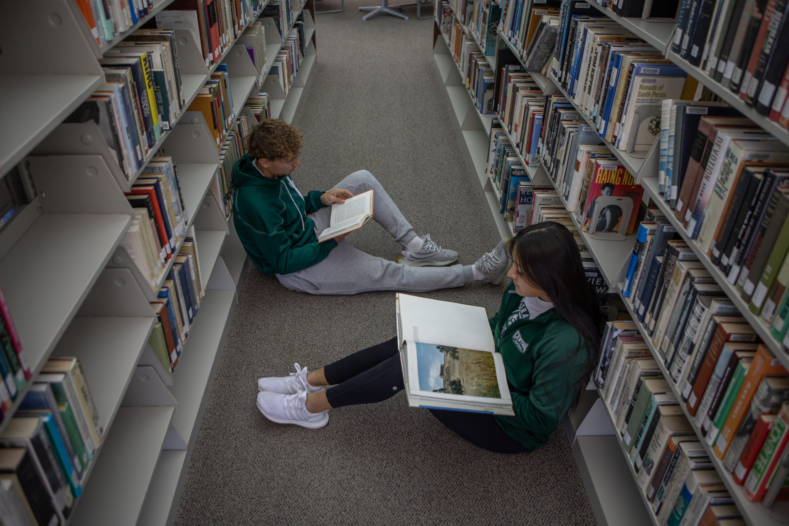 Two students sitting on the floor in library.