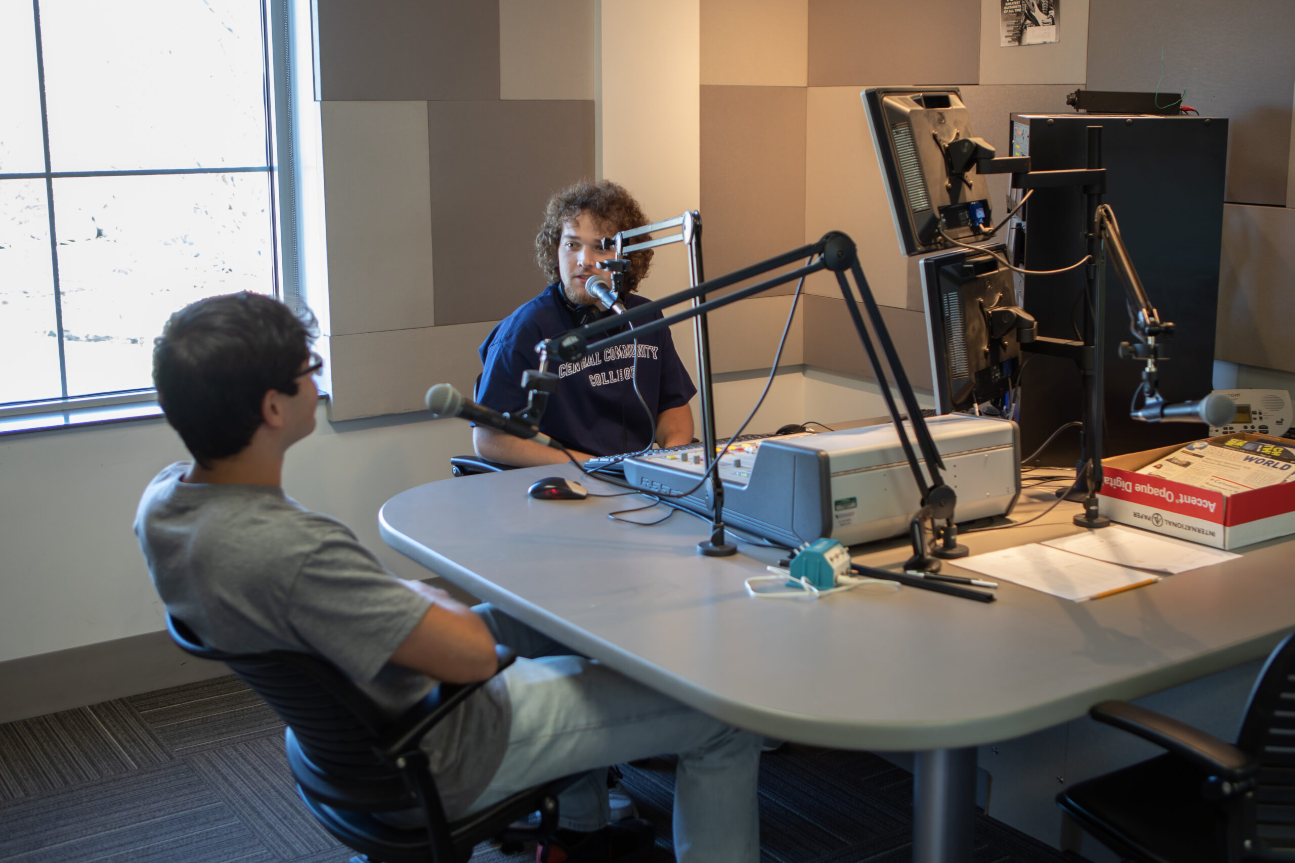 Two students sitting around podcast equipment.
