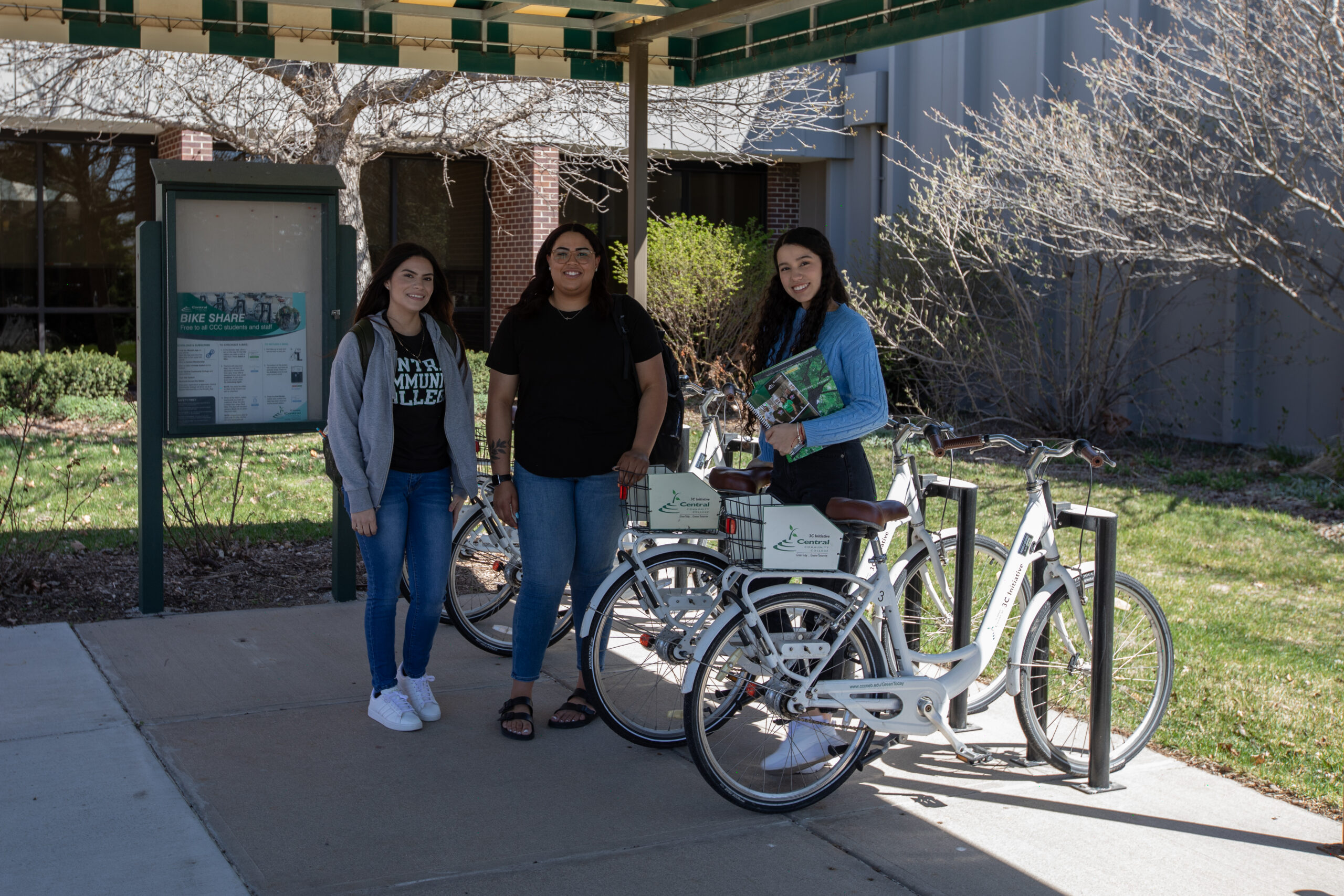 Three students outside, standing by bikes.