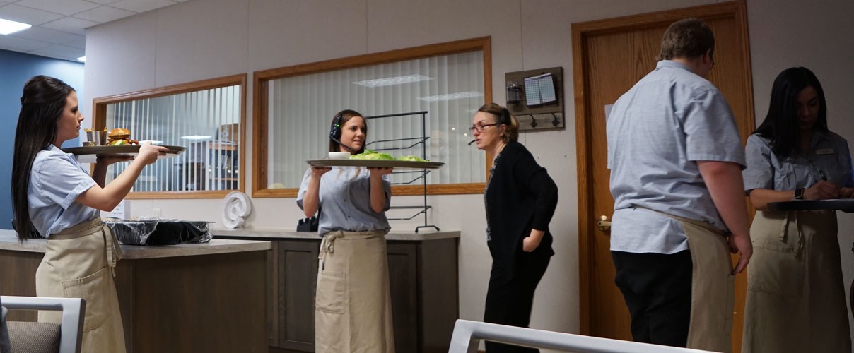 Restaurant management students serving food to dining tables.