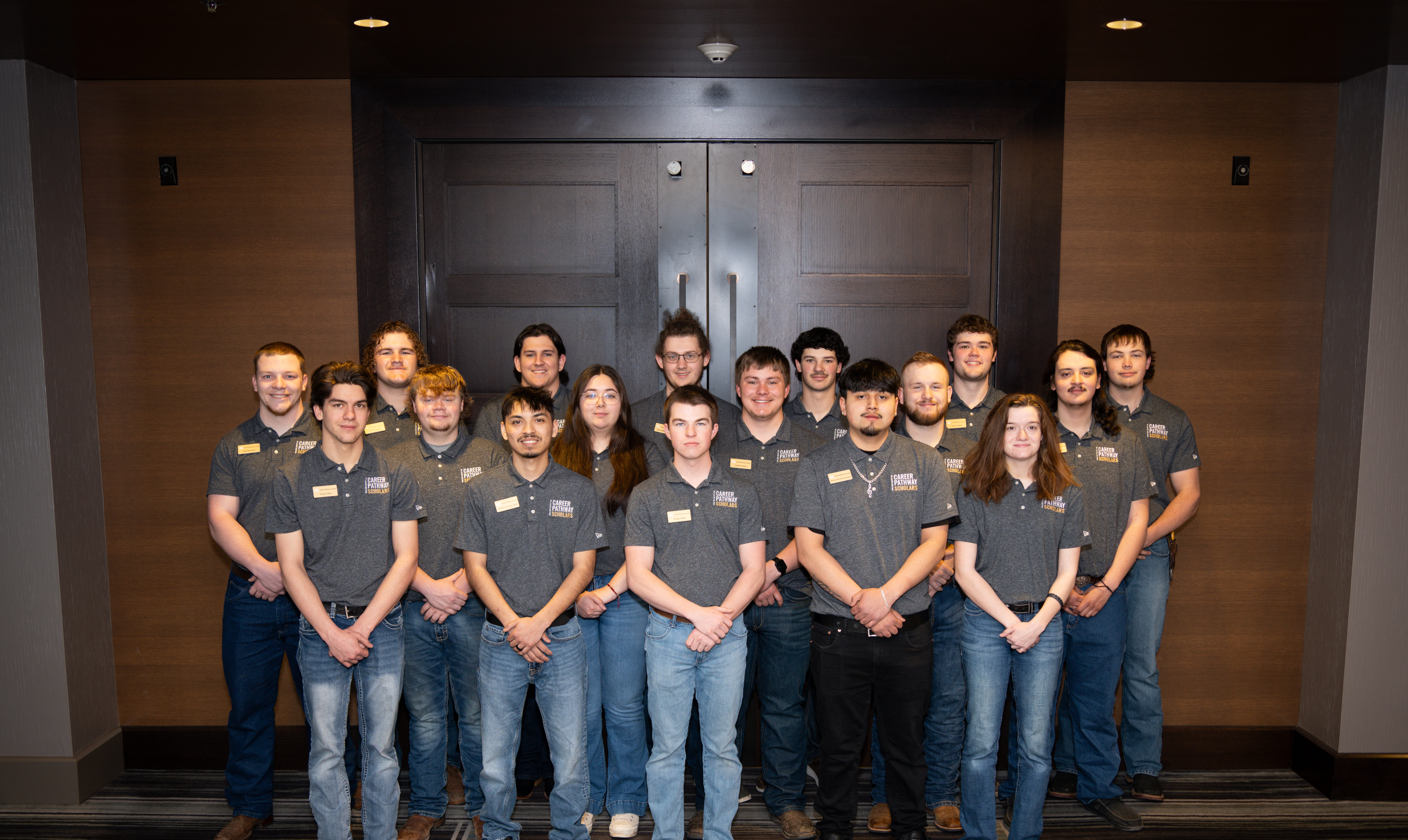 Large group wearing matching shirts poses indoors in front of double doors.