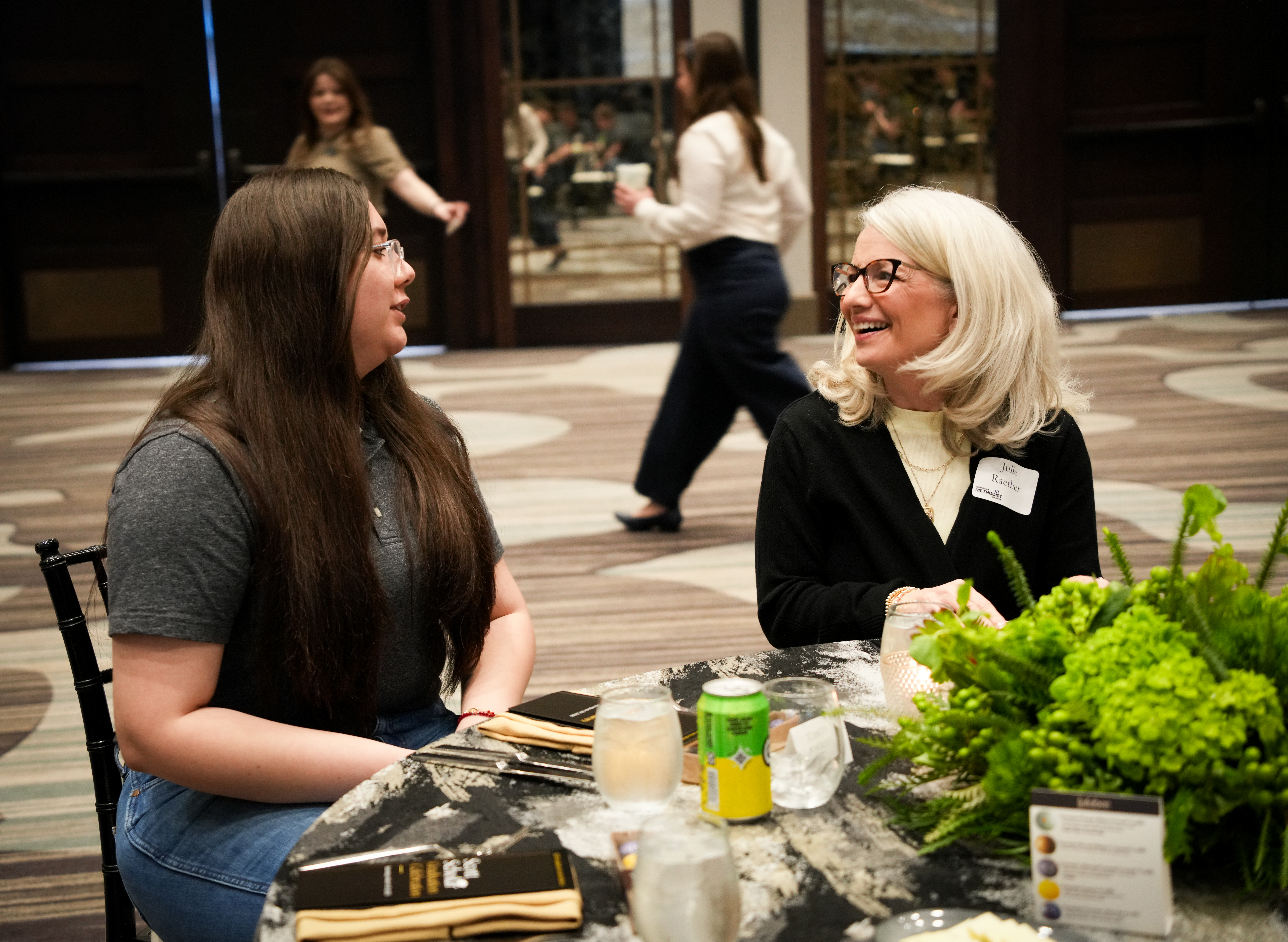 Two people sit at a decorated table talking during a formal networking event.