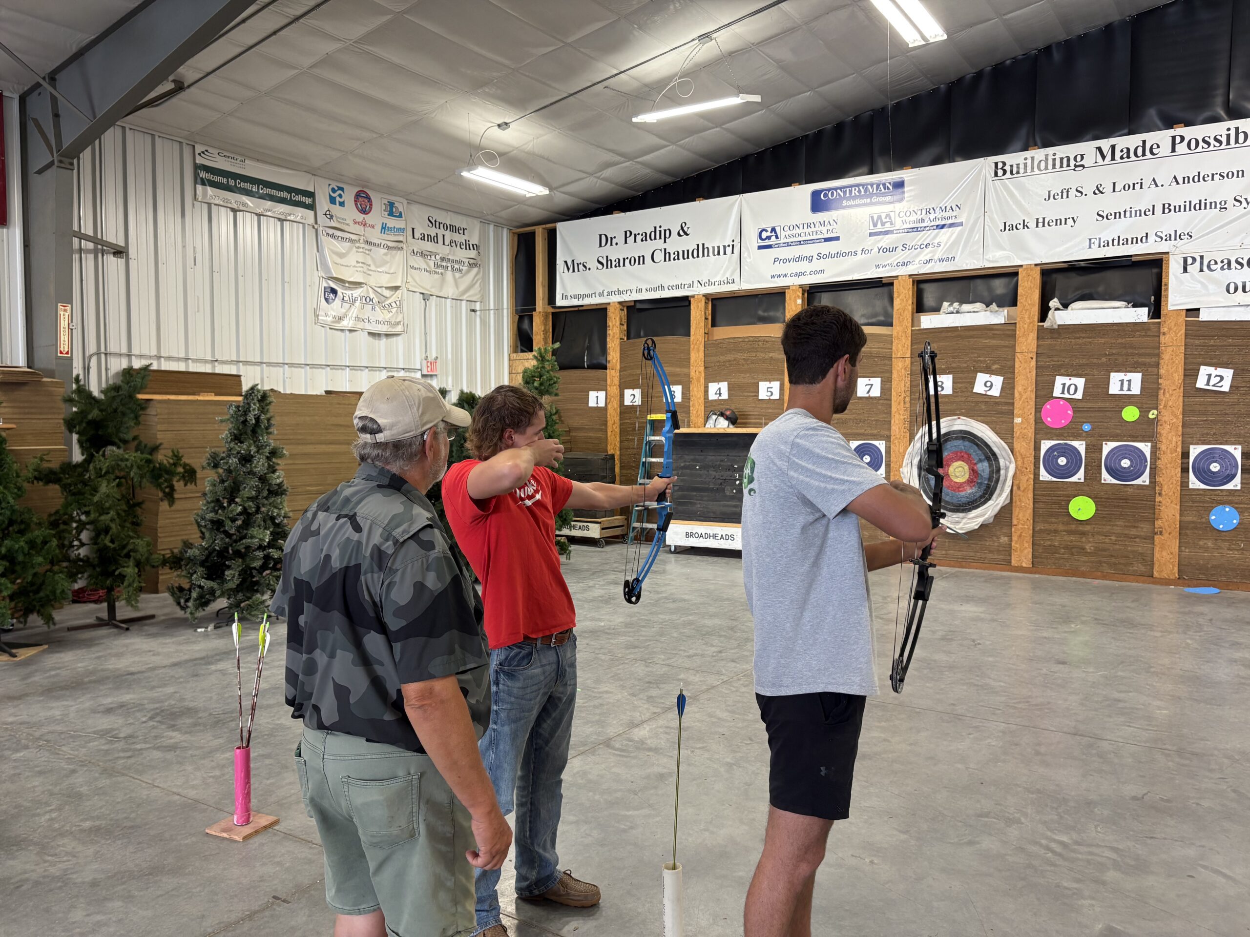 Participant practices archery indoors while an instructor observes nearby.