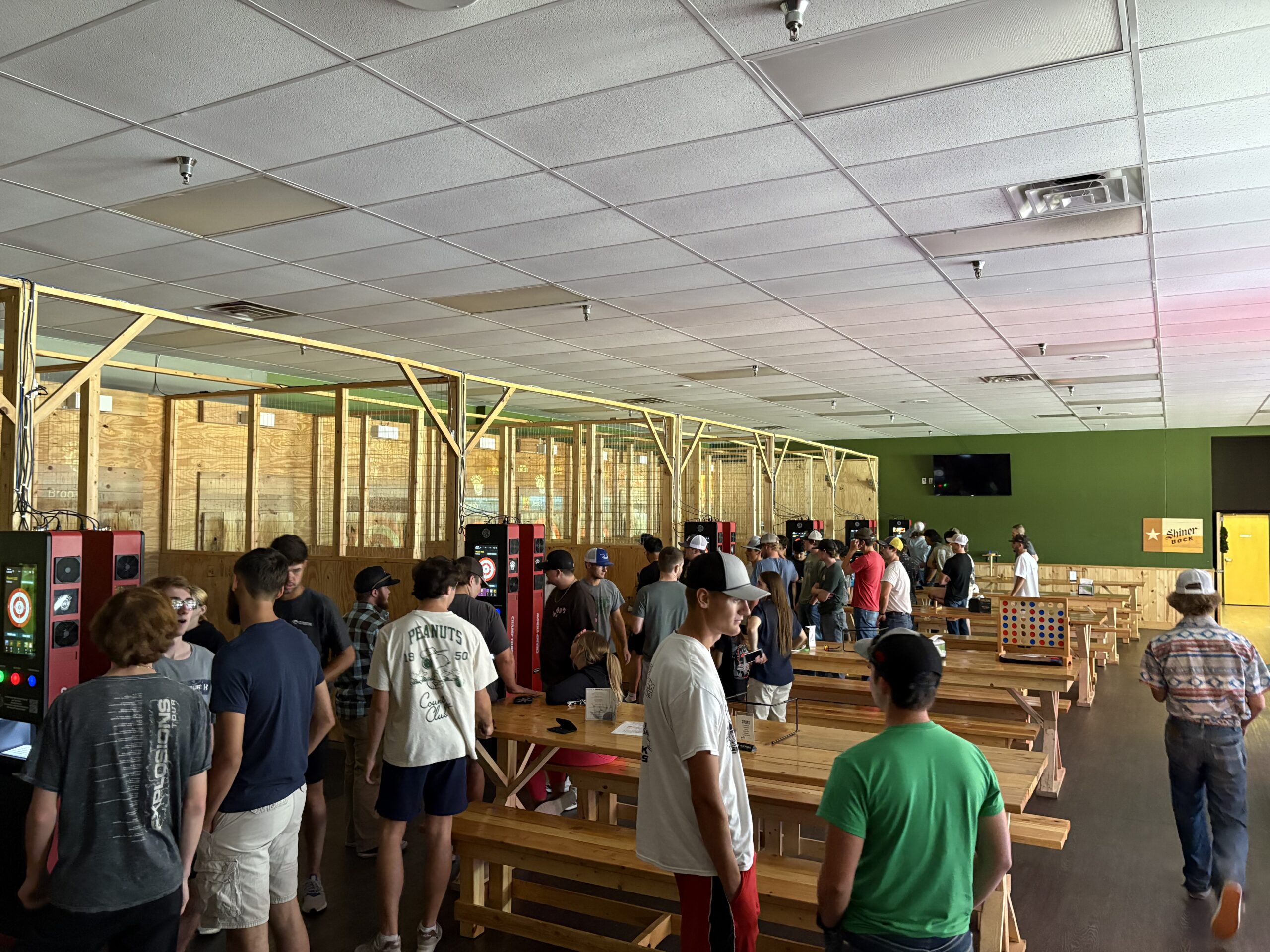 Crowded indoor venue with people socializing near wooden game lanes and tables.