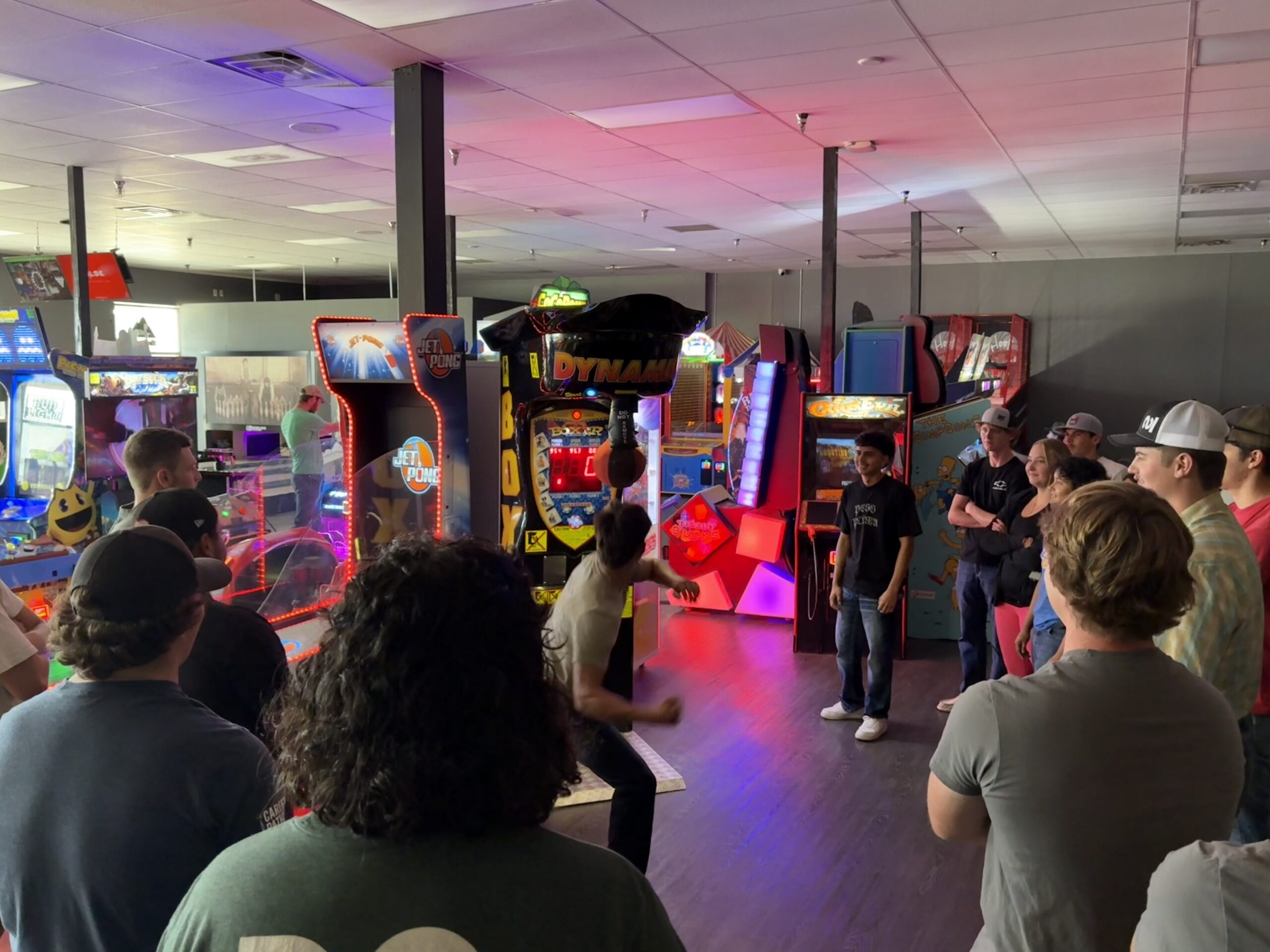 Group gathered in a neon-lit arcade with classic game cabinets and a central pillar.