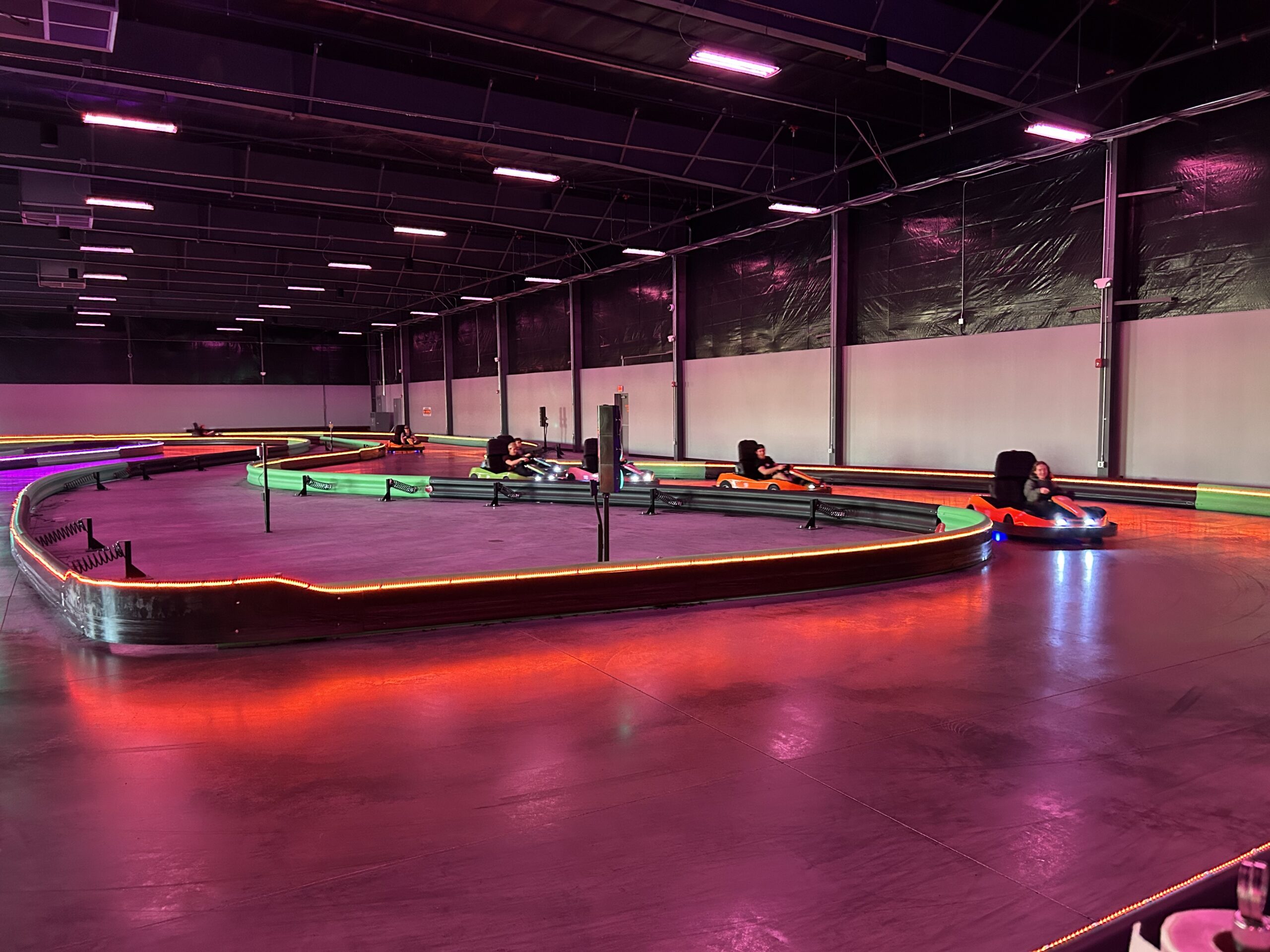 Indoor go-kart track with racers driving illuminated karts around a curved course.