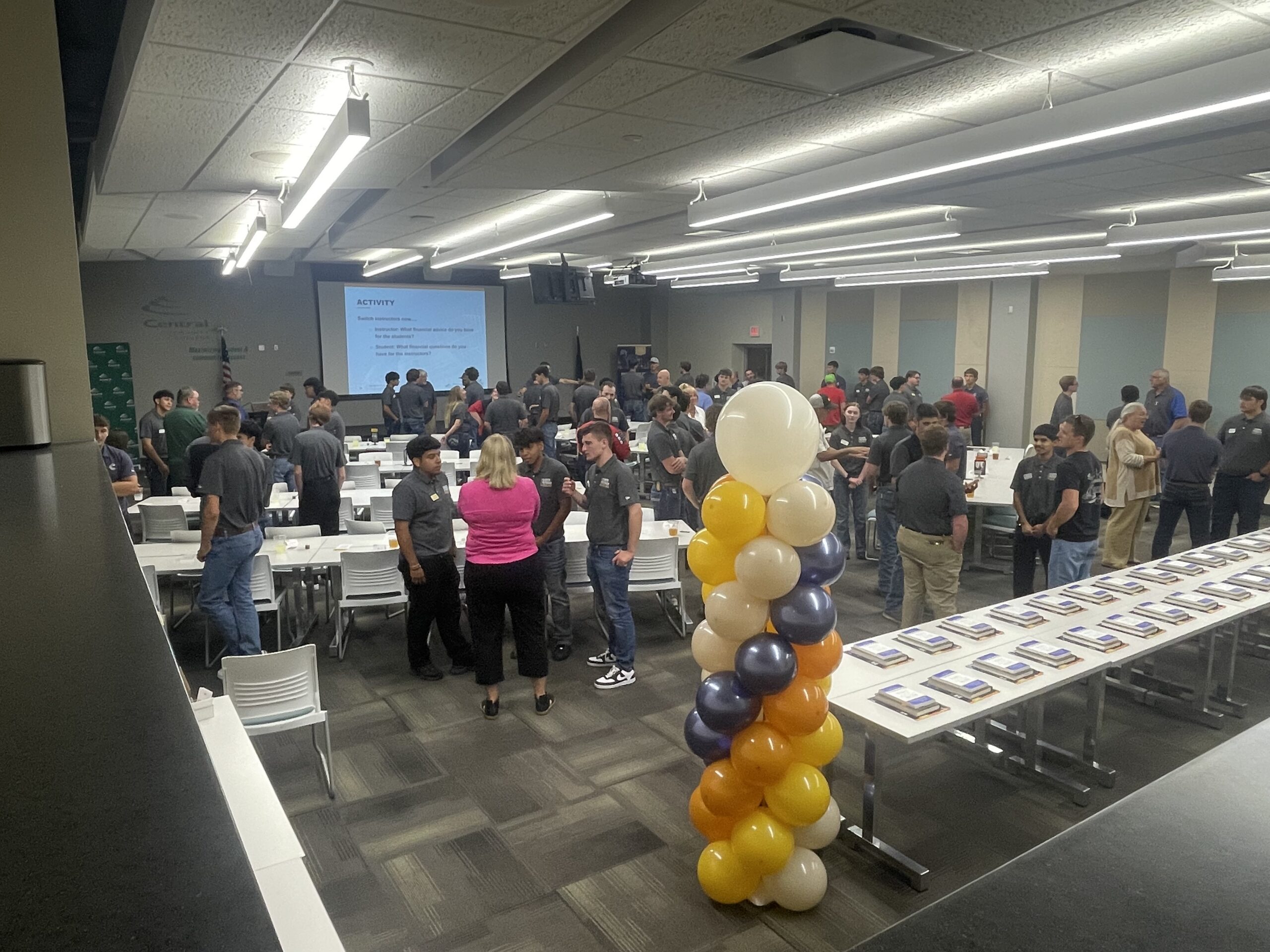 Large group of students networking in a conference room with tables and a balloon column.