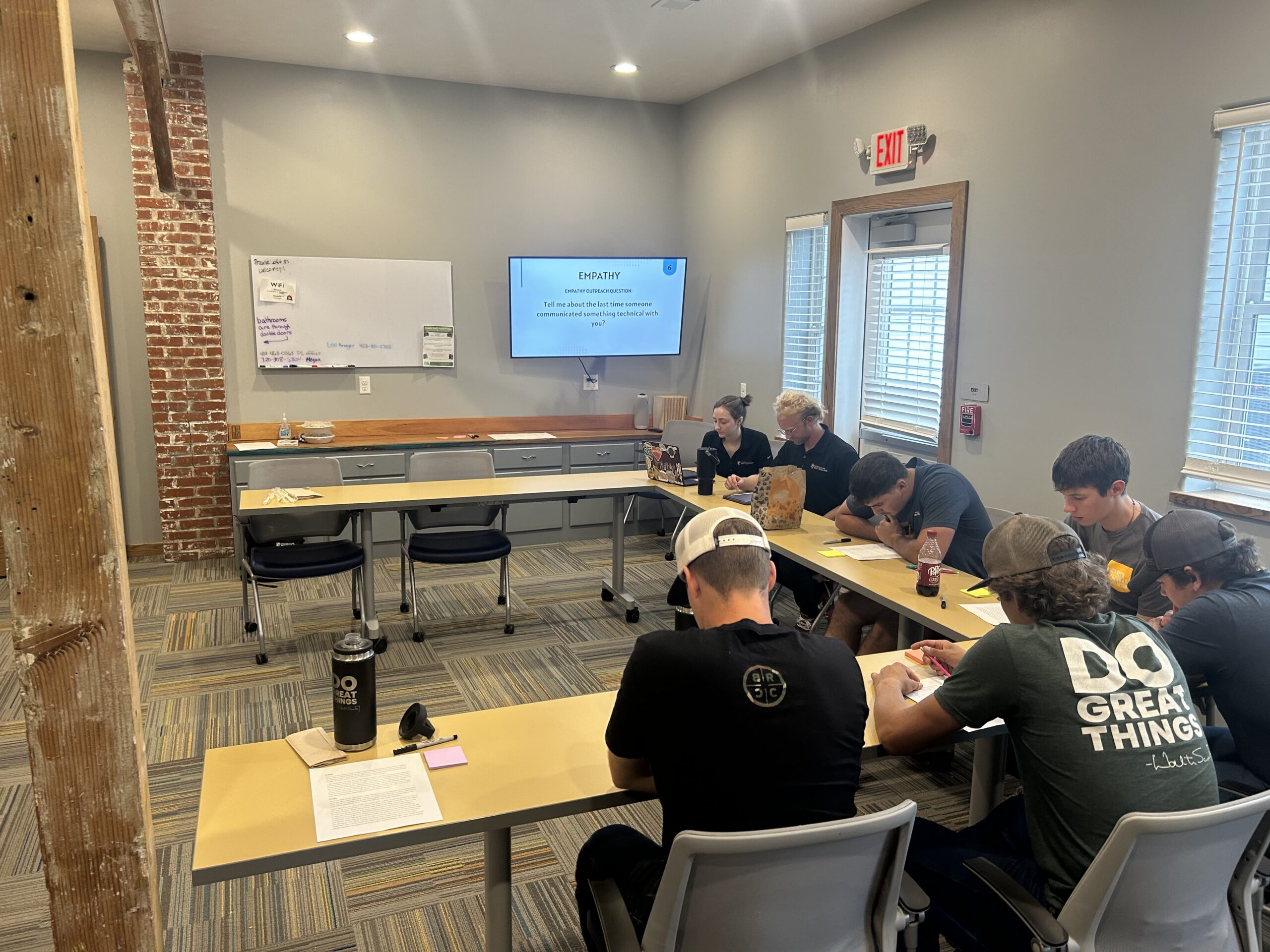 Students sit at U shaped table in a classroom with a screen at the front.