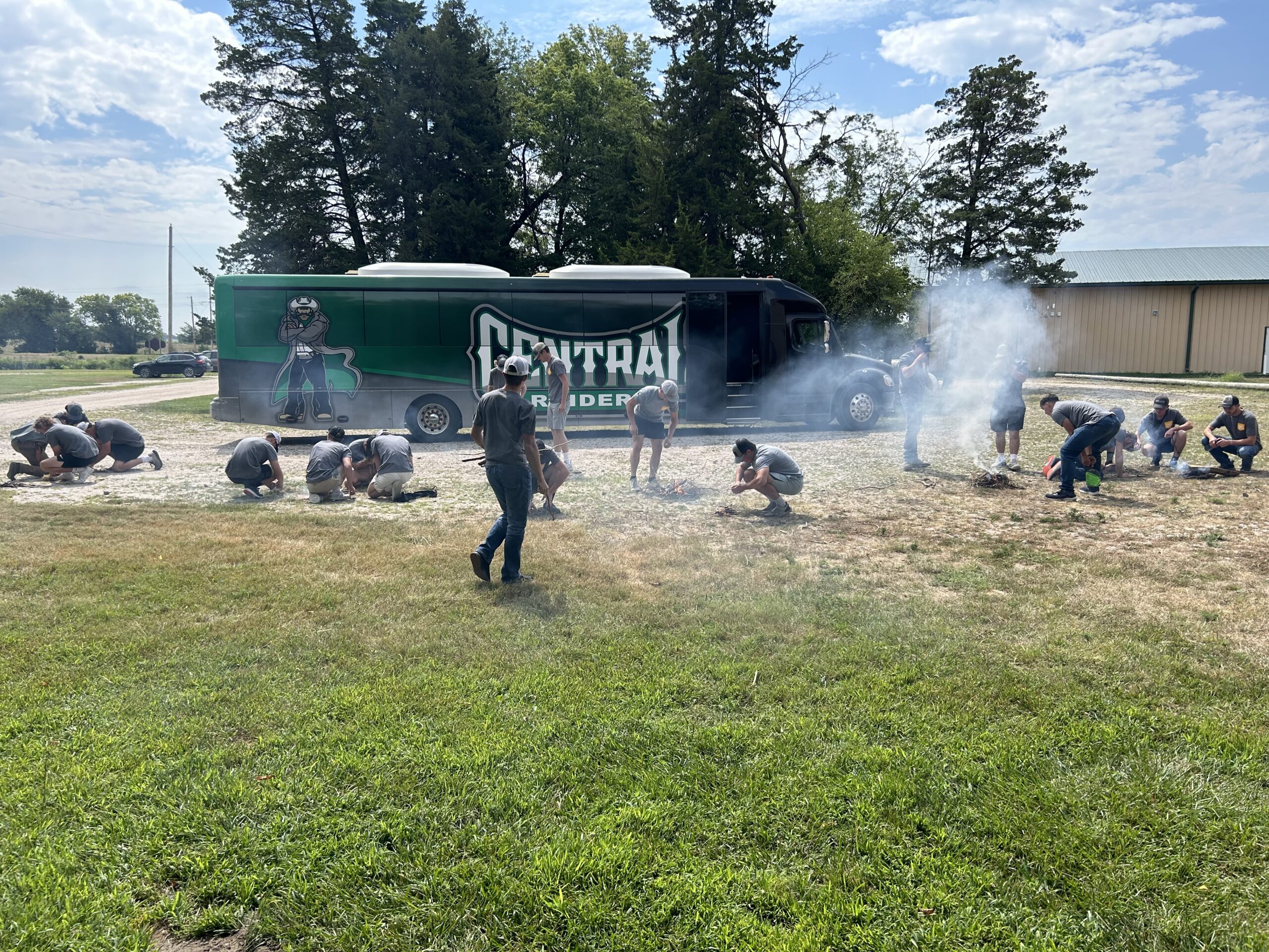 Group participates in outdoor team-building exercise near a bus on a grassy field.