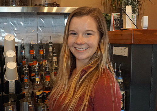 Michaela Frederick, standing in front of flavoring syrups at coffee shop.