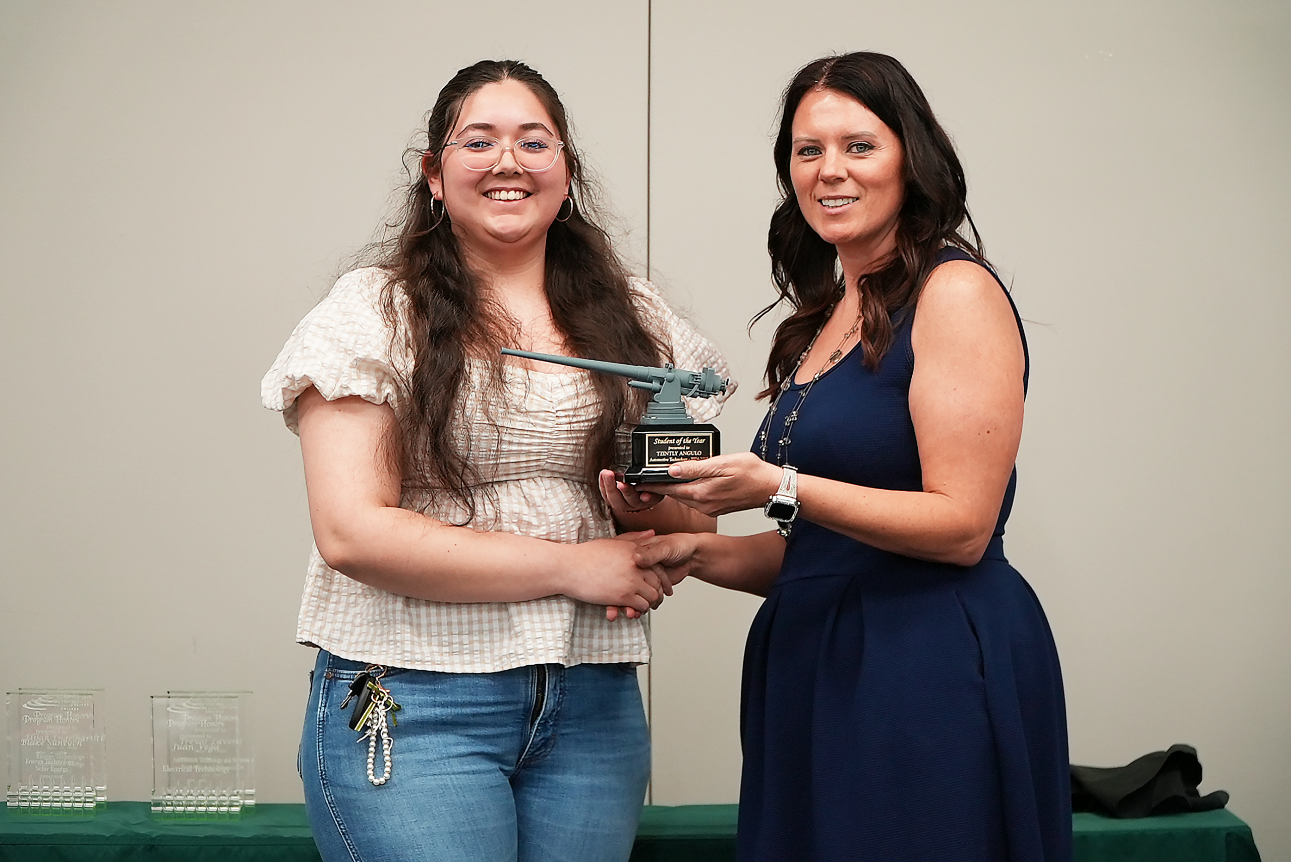 Two people pose while holding an award trophy at an indoor event.