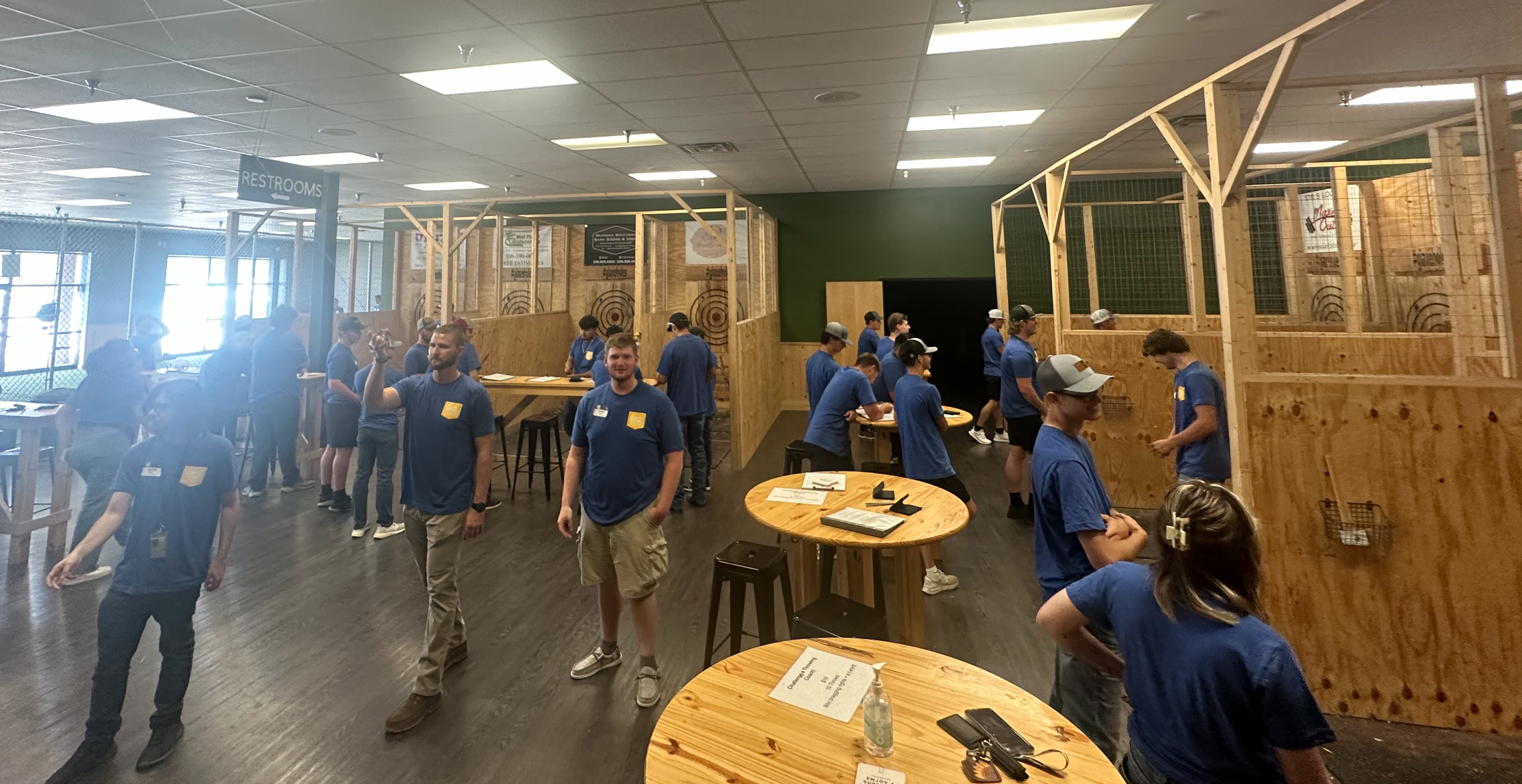 People socialize inside an indoor axe throwing venue with wooden targets.