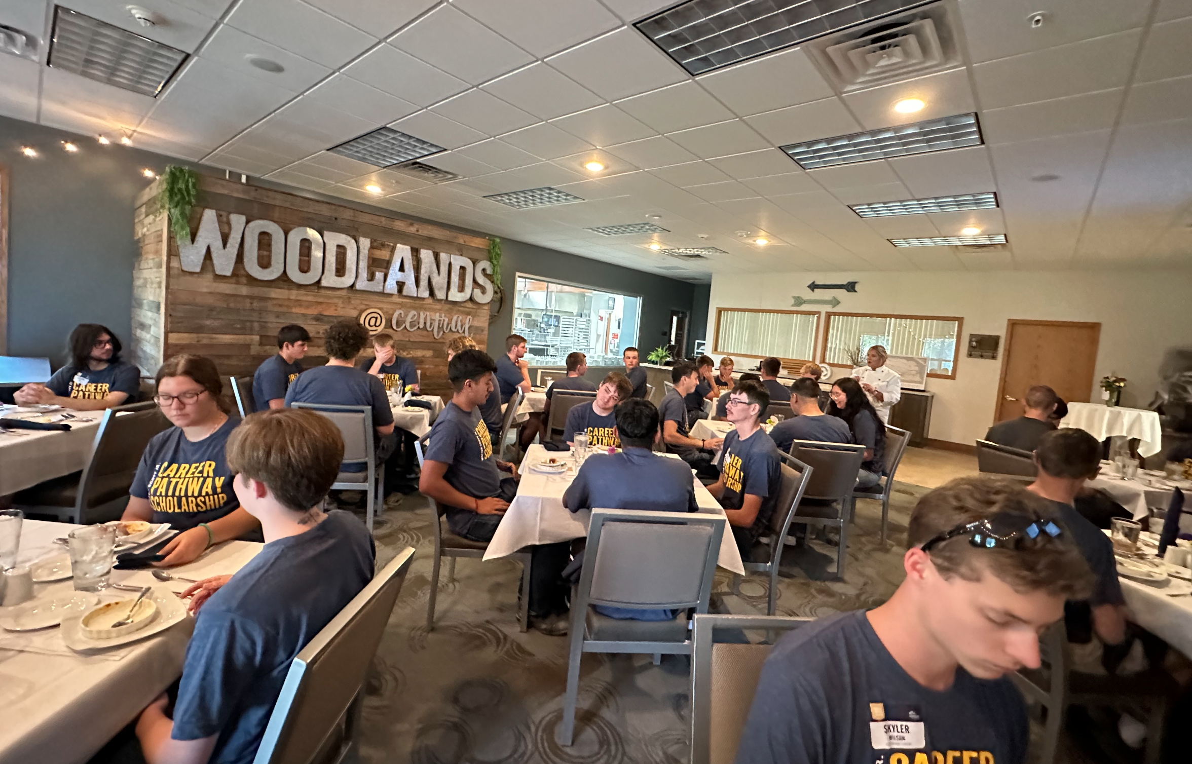 Group dining together in a restaurant with Woodlands at Central signage.