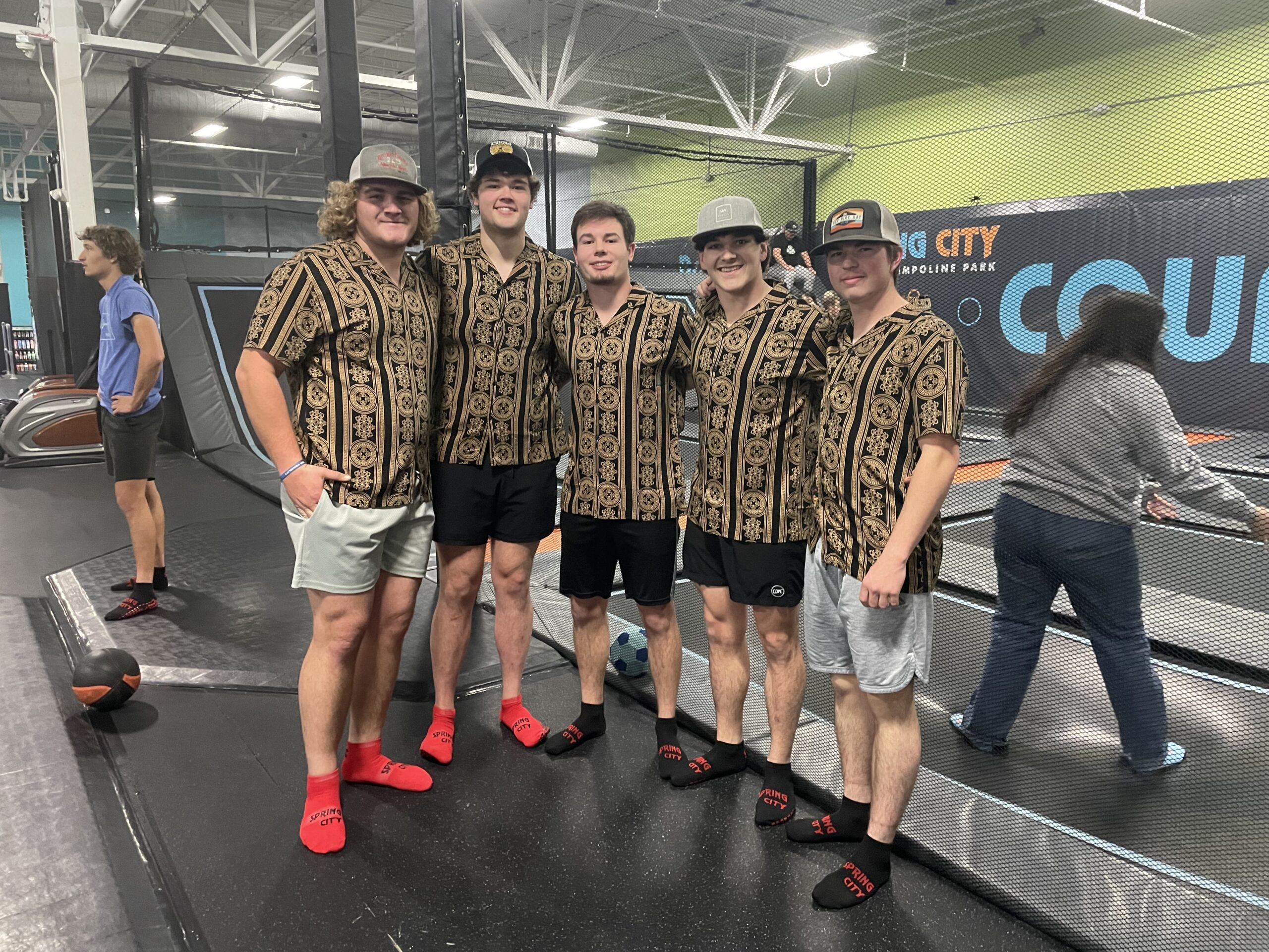Five people wearing matching shirts stand together inside a trampoline park.