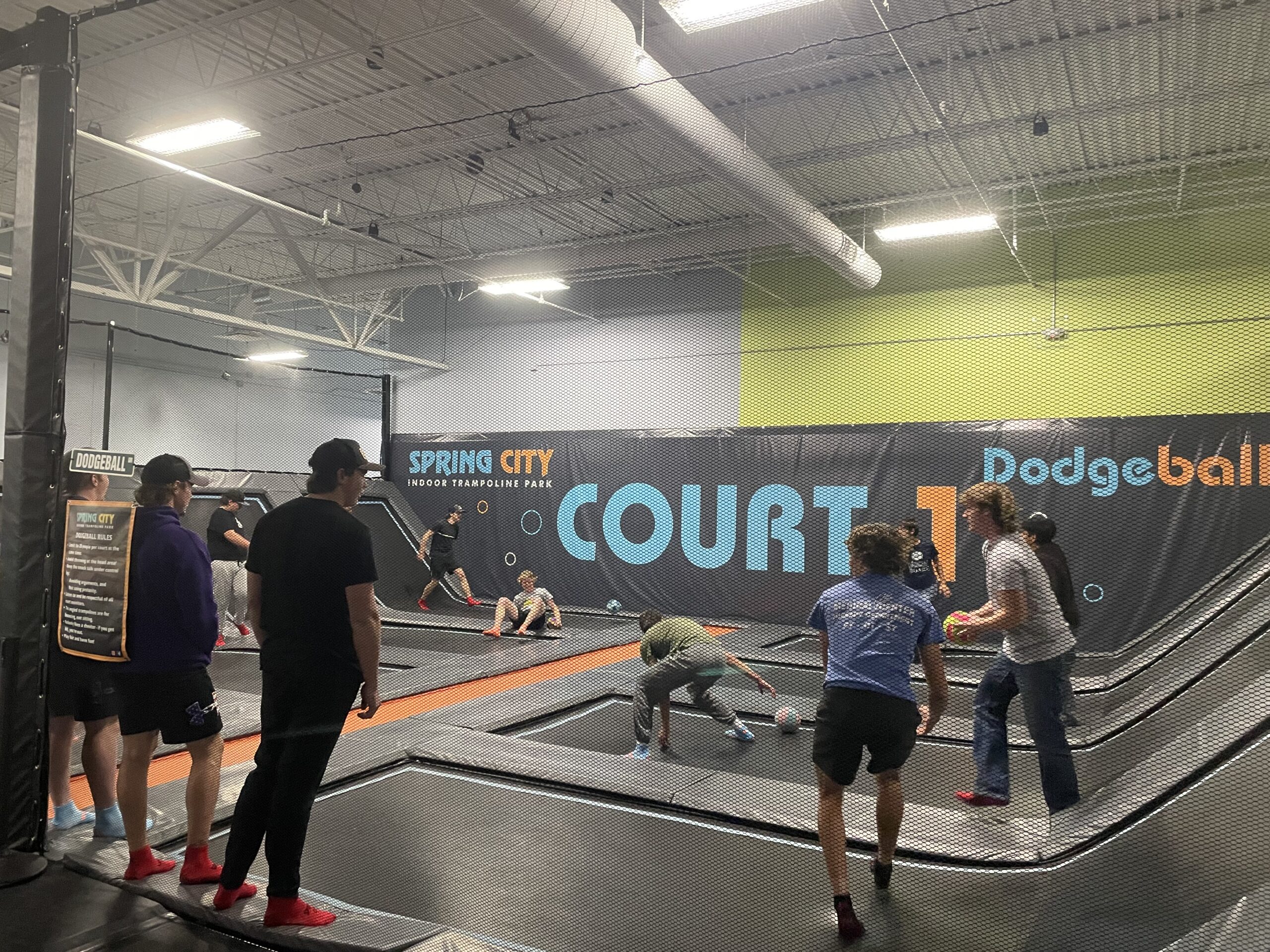 People play dodgeball on trampolines inside an indoor recreation facility.