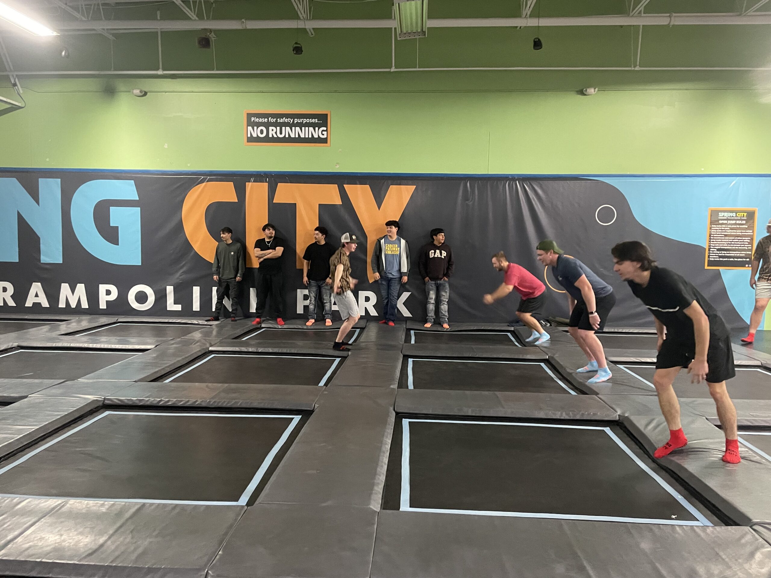 Group jumps and runs across adjacent trampolines under a “No Running” sign.